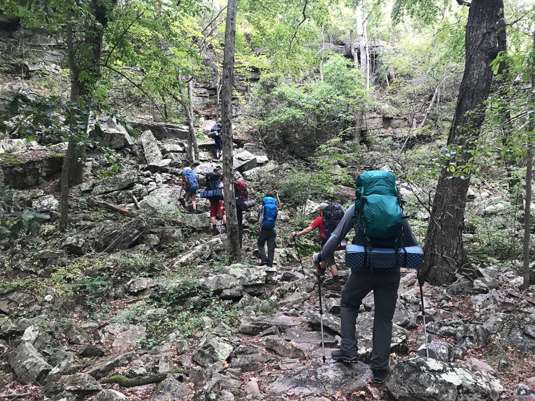 Hikers make their way up a rocky, forested trail