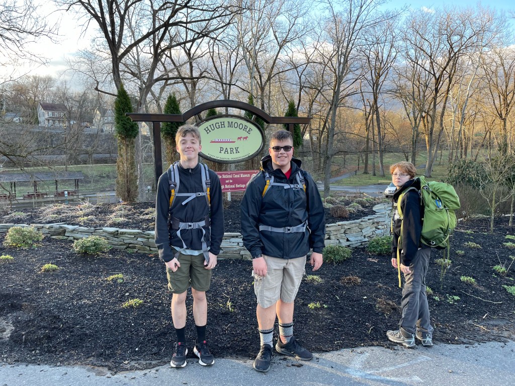 Three scouts in backpacks and jackets prepare to head out on the trail.