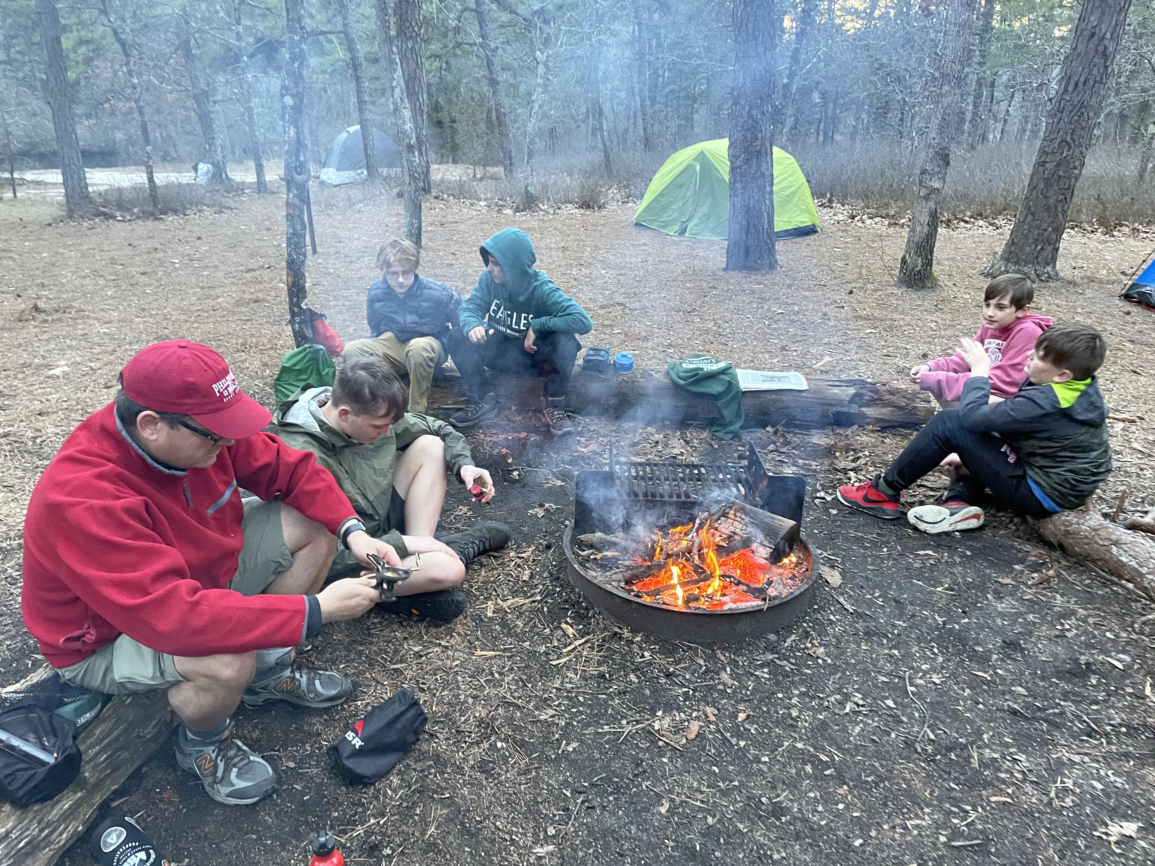 A group of scouts and adults are gathered around a fire.