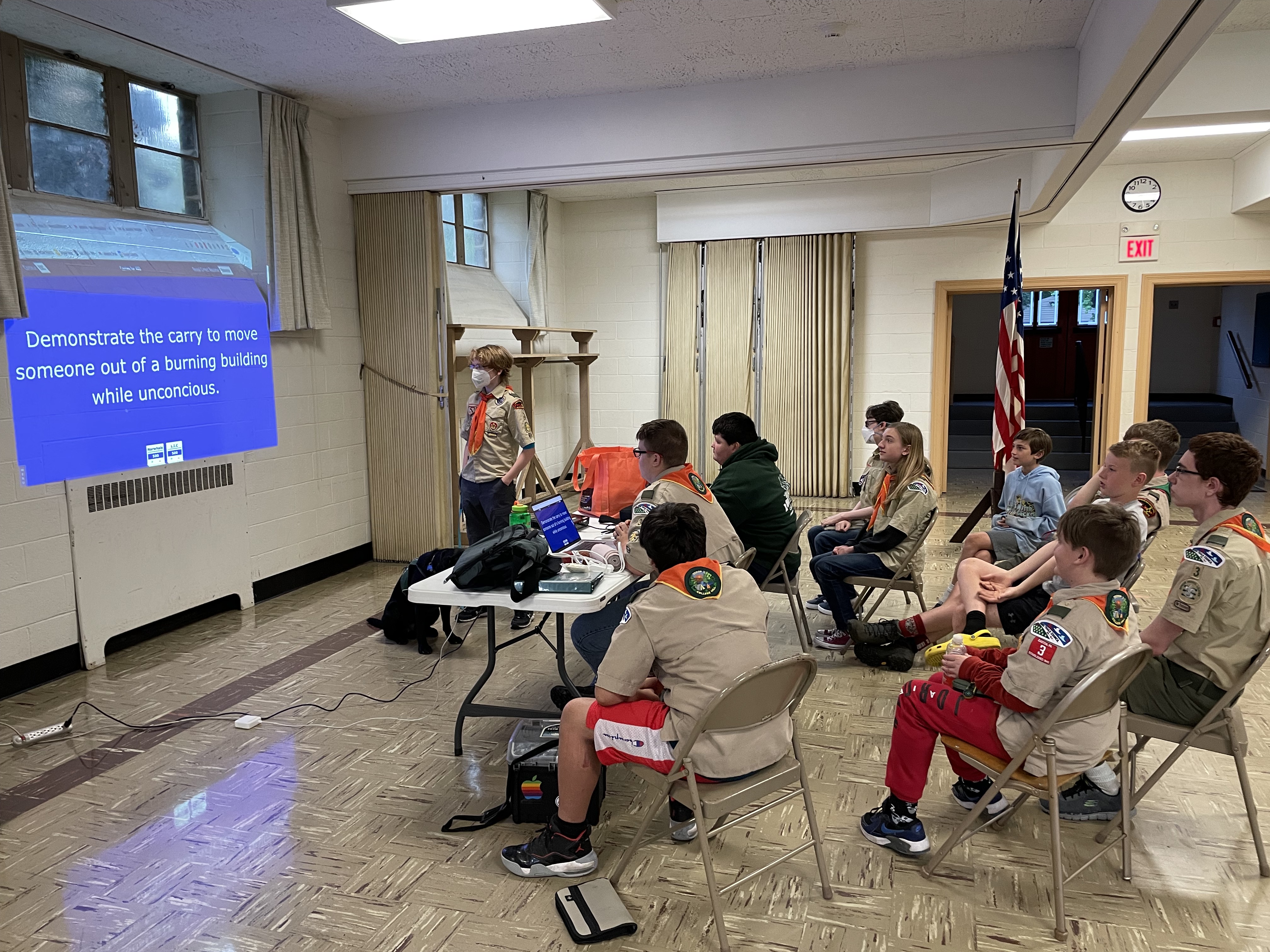 A group of seated scouts reads a question project onto a screen as part of a scout meeting.